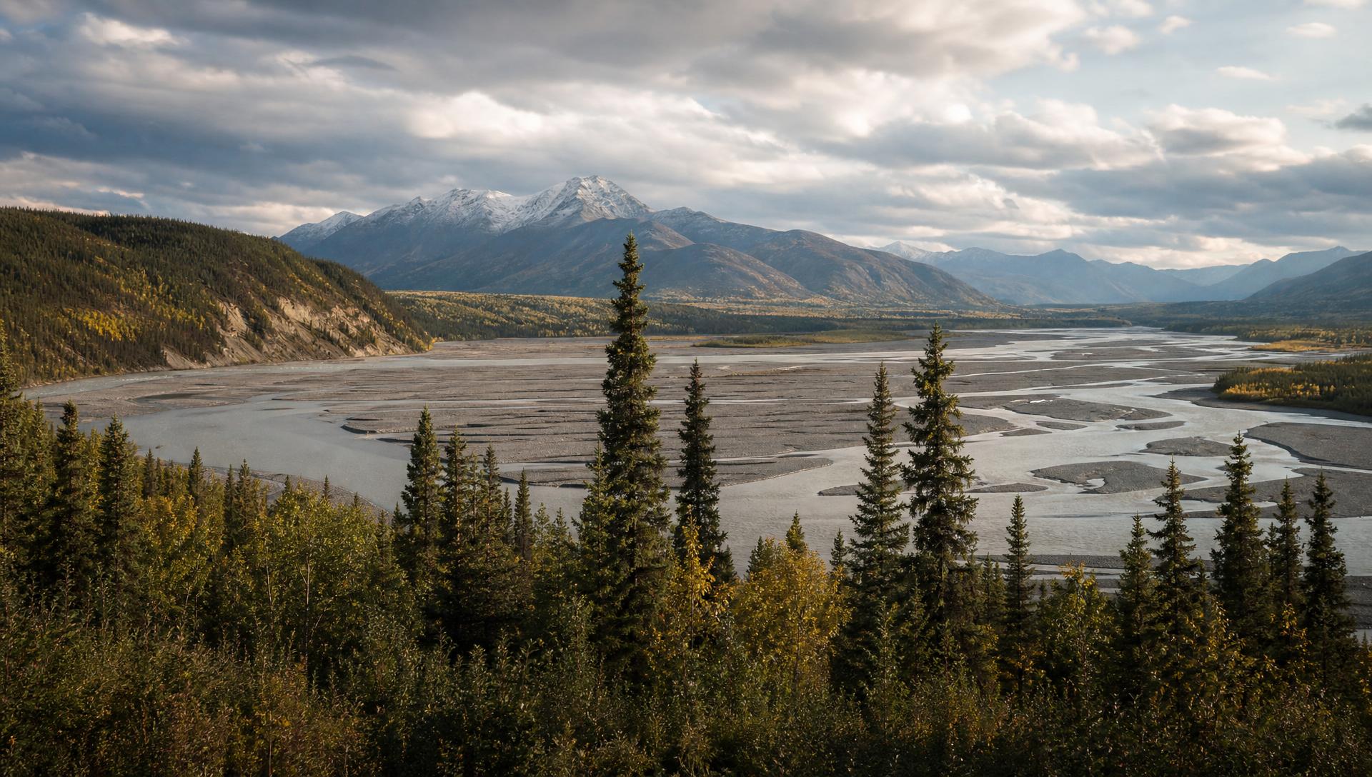 Golden hour over a Yukon mountain range with a braided glacial river winding through the valley